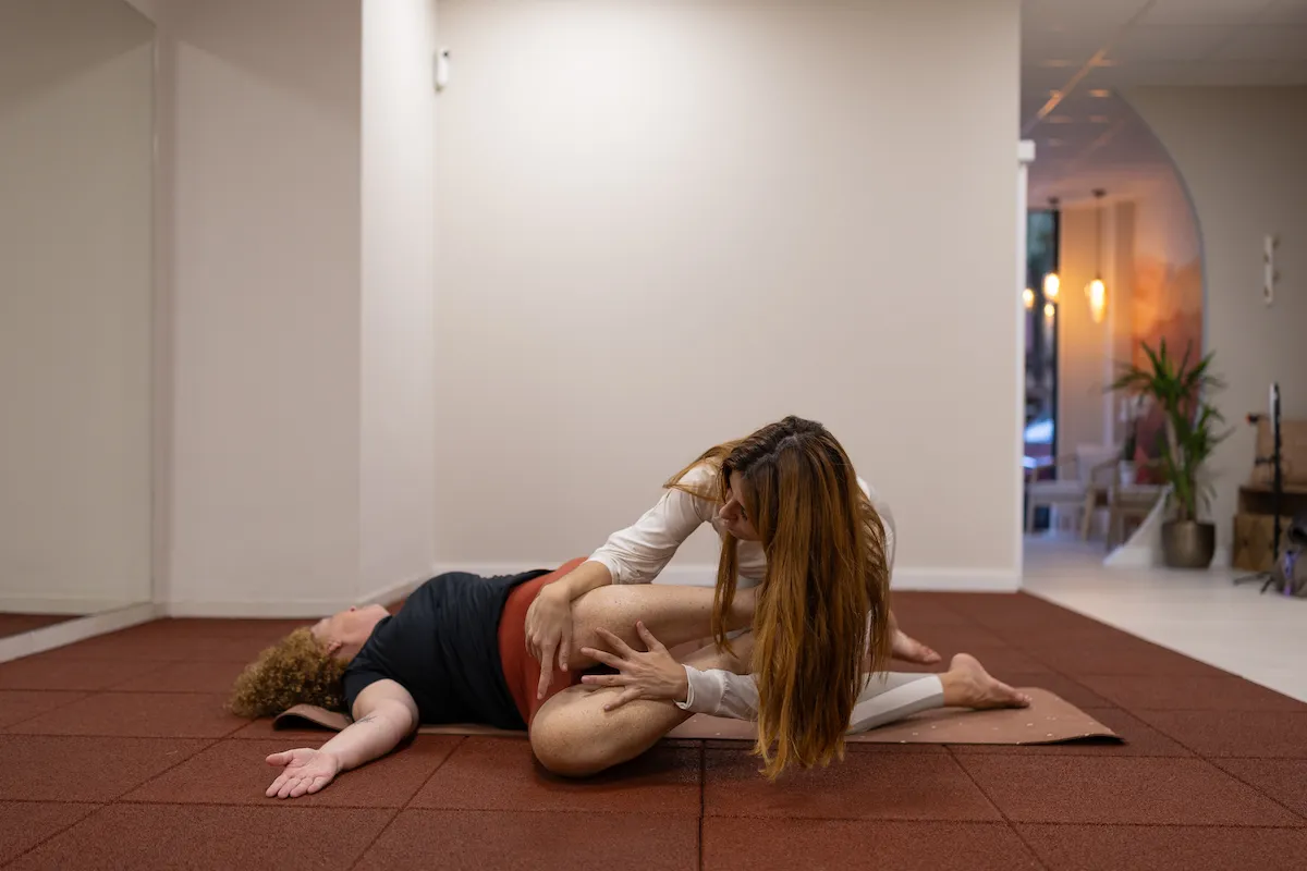 Fisioterapeuta realizando técnica de estiramiento asistido en el suelo con una paciente durante una sesión de tratamiento del dolor.